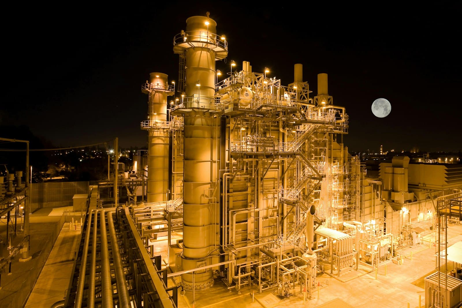 An industrial power plant illuminated at night with a full moon in the sky